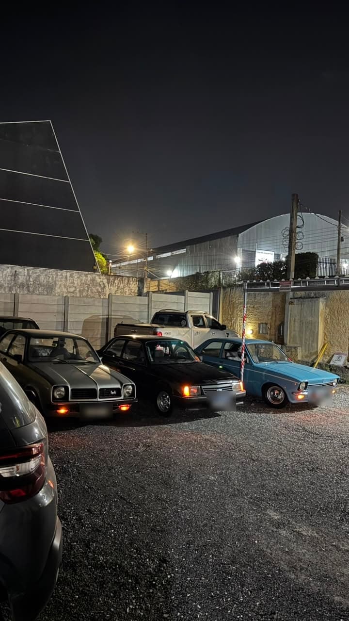 Encontro de carros antigos à noite, com vários modelos enfileirados no pátio sob luz artificial